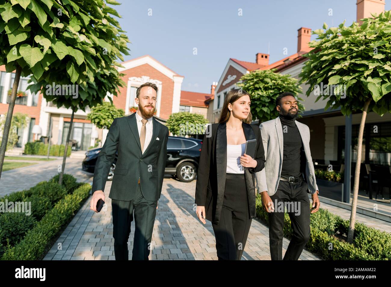 equipo de gente de negocios multiétnica dos hombres y mujeres con ropa  informal elegante, caminando al aire libre en la reunión de negocios. La  mujer sostiene la tableta digital Fotografía de stock -