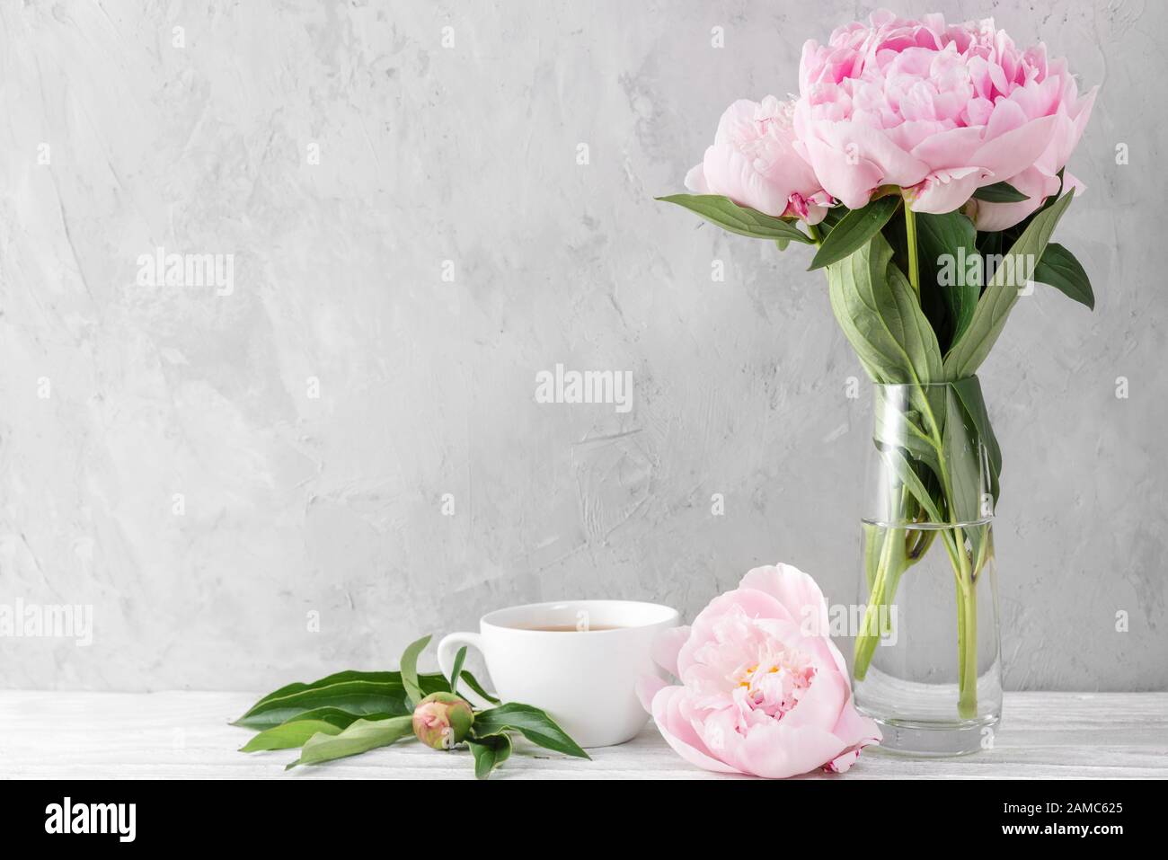 Ramo de flores de peonías rosa con taza de café sobre mesa blanca con  espacio para copiar. Vida fija. Fondo para el día o la boda de las mujeres  Fotografía de stock -