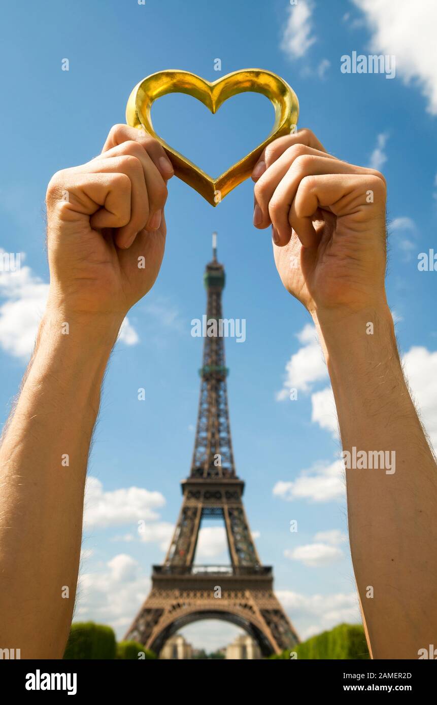 Manos sosteniendo golden heart afuera encima de una vista de postal de la Torre Eiffel en Paris, Francia Foto de stock