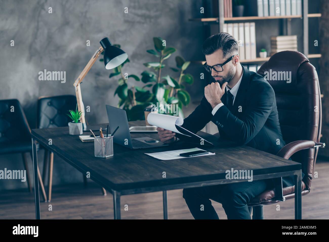 Foto de perfil de guapo hombre de negocios leyendo informe de papel sujetando la mano en la barbilla considerado documentos importantes desgaste especificaciones negro blazer camisa traje Foto de stock