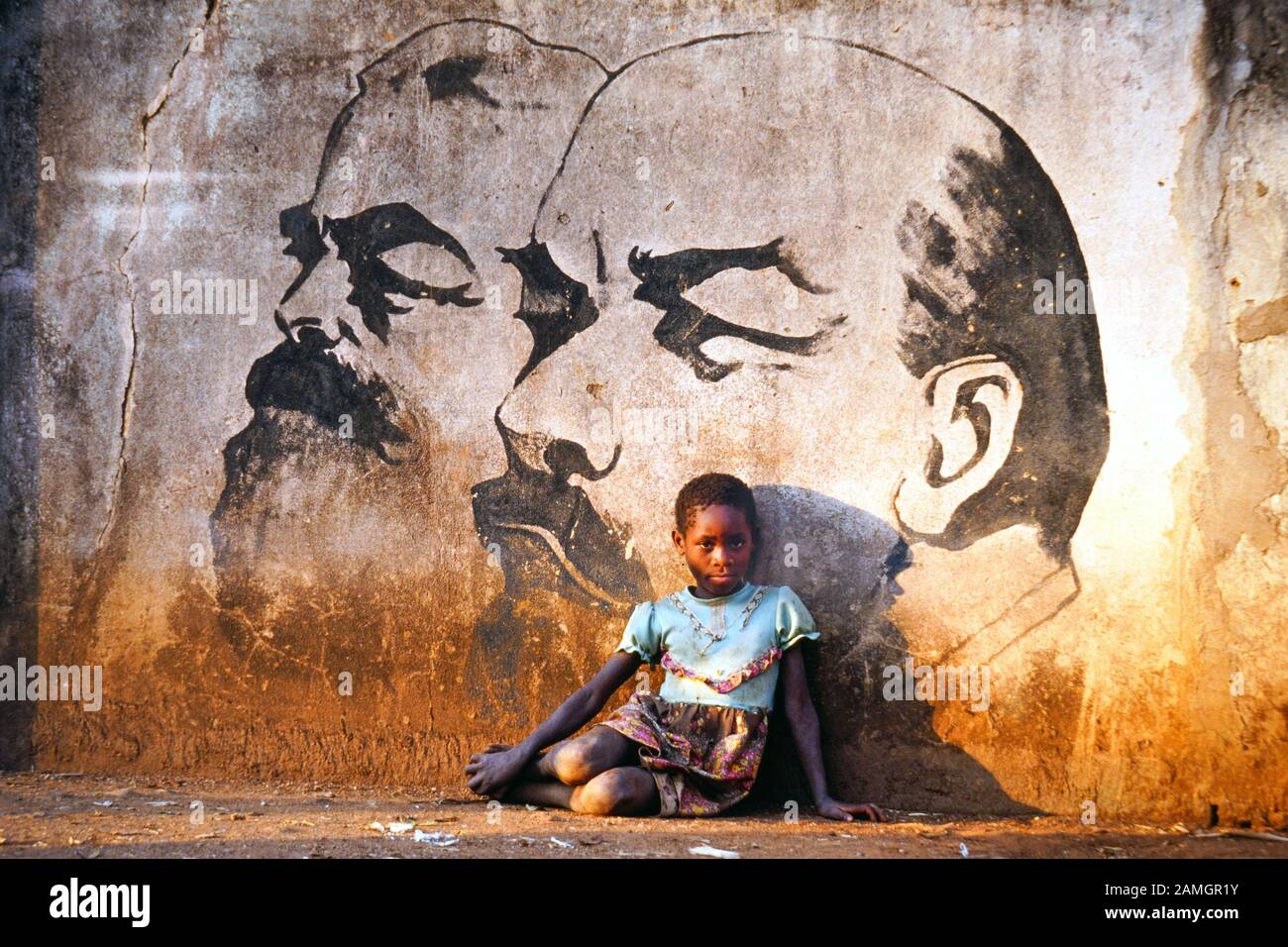 Foto vintage diapositiva de 35 mm de 1993: La niña africana se sienta frente a un cuadro mural que muestra a los líderes comunistas Marx y Lenin. Aldea de Quelimane en la provincia de Tete, Mozambique, África Foto de stock
