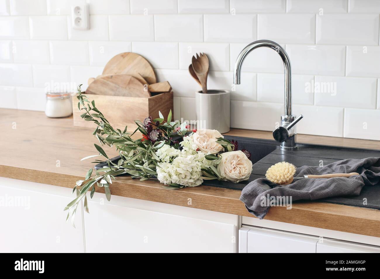 https://c8.alamy.com/compes/2amgxgp/primer-plano-del-interior-de-la-cocina-pared-de-ladrillo-blanco-baldosas-de-metro-encimeras-de-madera-con-utensilios-de-cocina-rosas-flores-en-lavabo-negro-escandinavo-moderno-2amgxgp.jpg