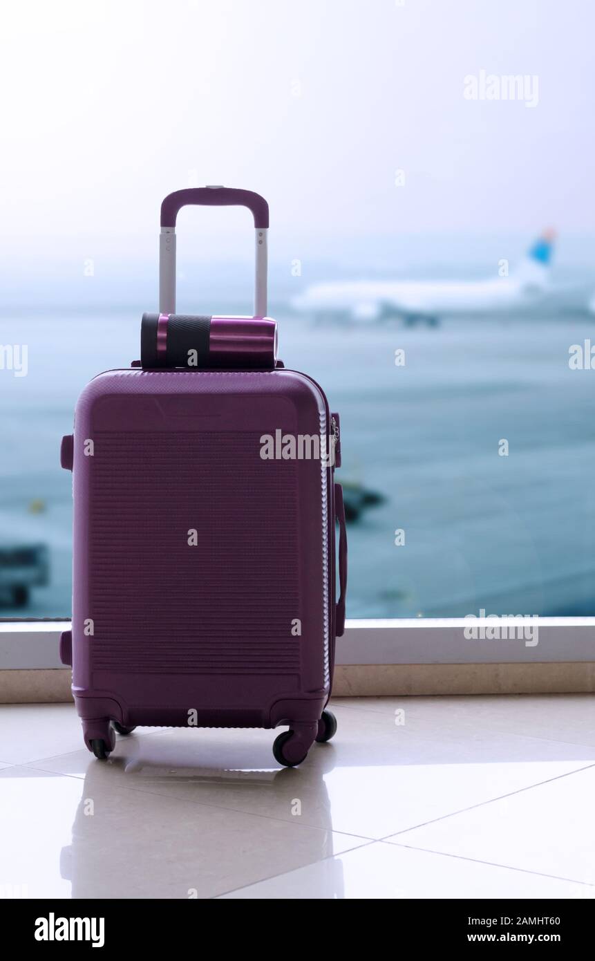 Foto concepto de viaje con maleta de plástico púrpura y termo copa en ella pista de aterrizaje del Fotografía de stock Alamy