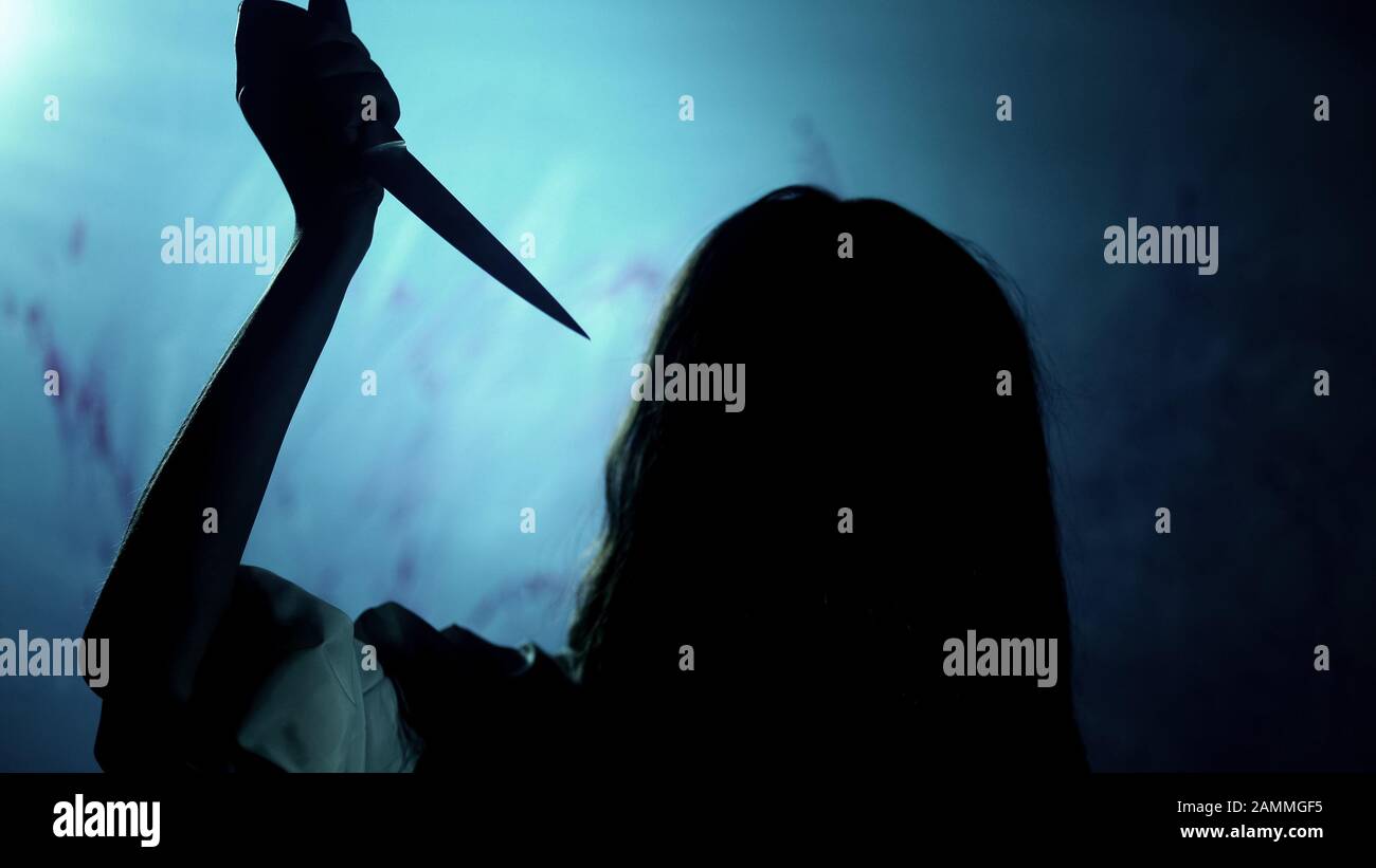 Sangriento asesino de cabello oscuro apesta a la víctima con cuchillo, oscuridad y horror Foto de stock