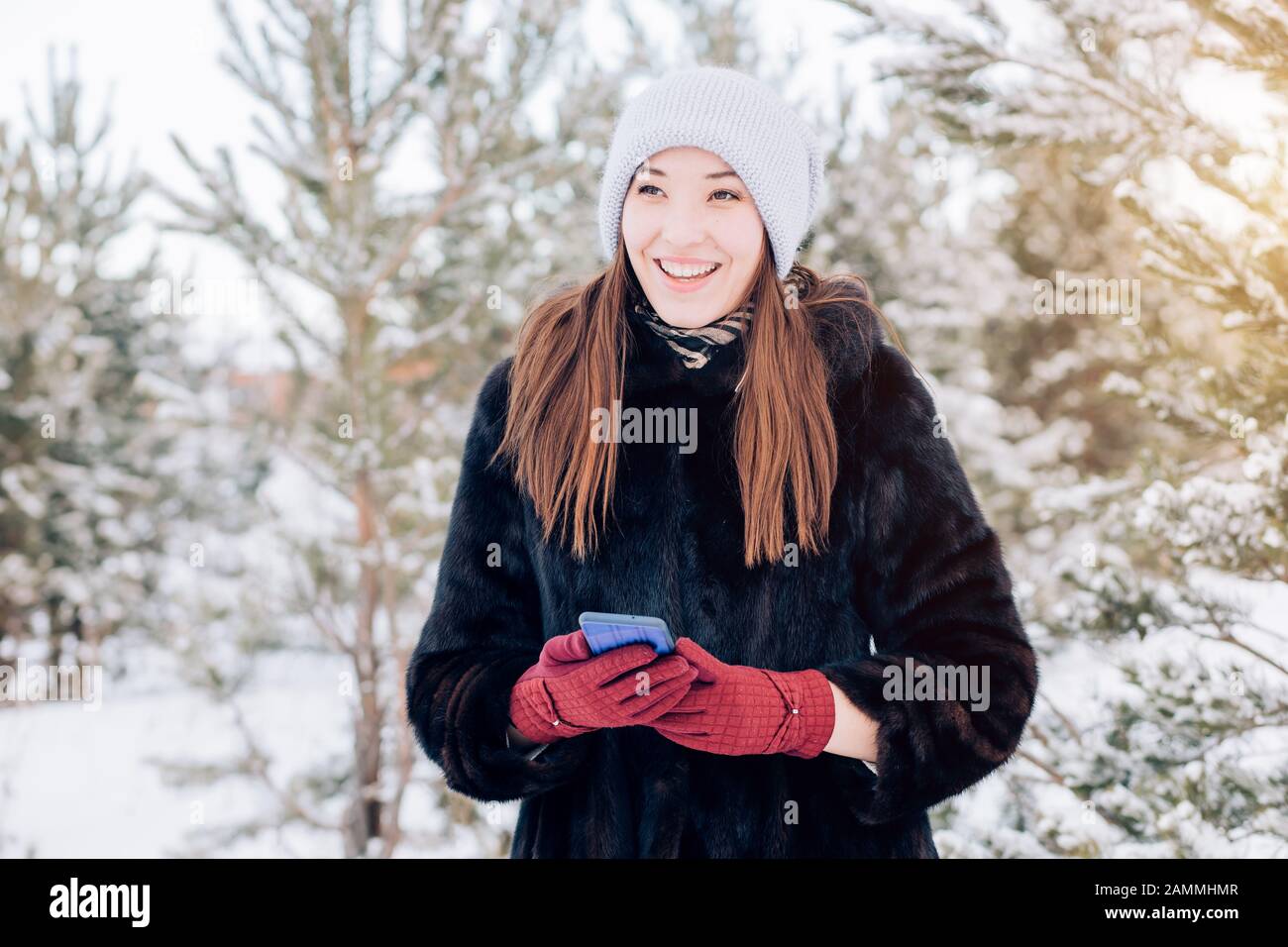 Hermosa mujer feliz sonriente en un abrigo de piel cálido, sombrero de  punto, guantes rojos sosteniendo un smartphone en su mano y sonriendo  mirando hacia el backgr Fotografía de stock - Alamy