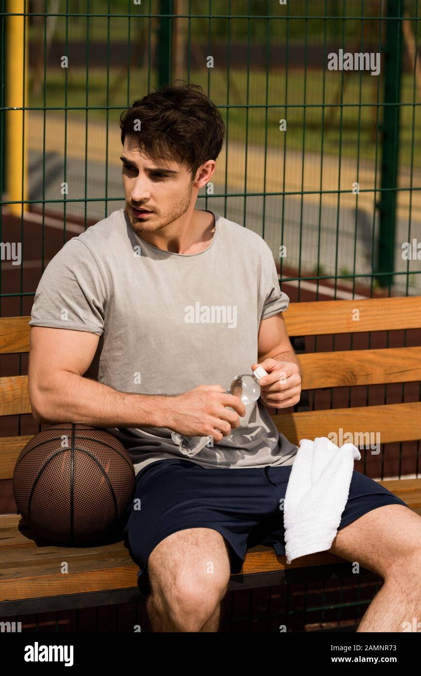 jugador de baloncesto sentado en un banco de madera y sosteniendo una toalla  y una botella de agua en la cancha de baloncesto Fotografía de stock - Alamy
