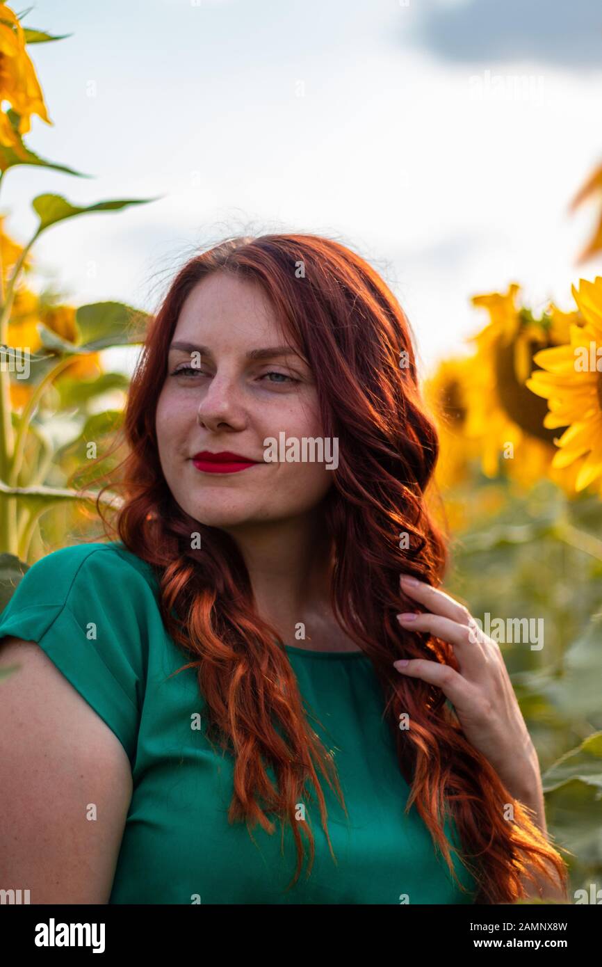 Hermosa joven con cabello rizado rojo y un vestido verde posando en un  girasoles fieldon un día soleado en verano Fotografía de stock - Alamy