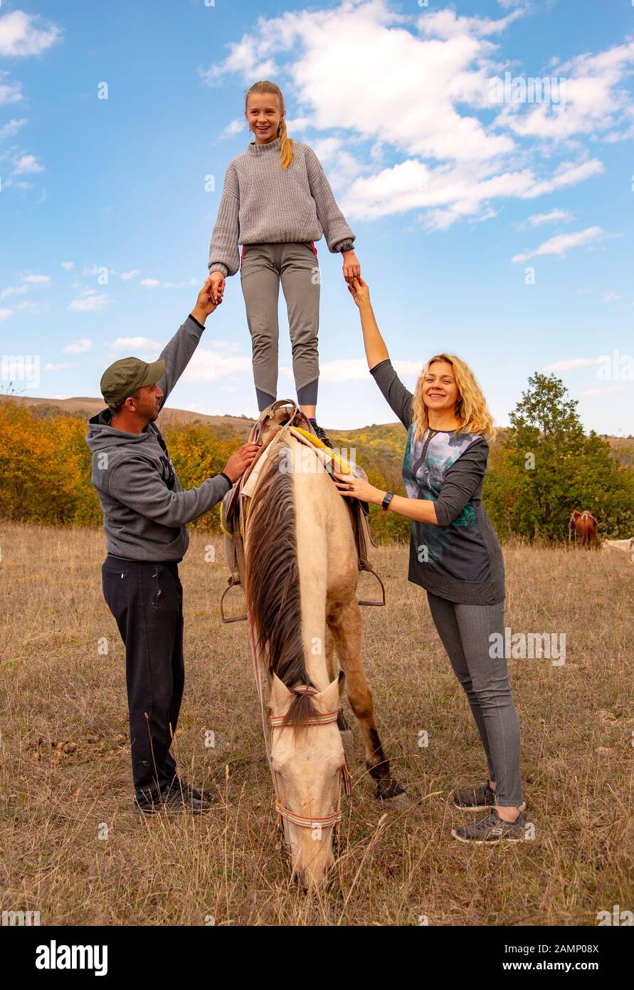 Una niña adolescente se encuentra en un caballo, apoyada por adultos a ambos lados. Foto de stock