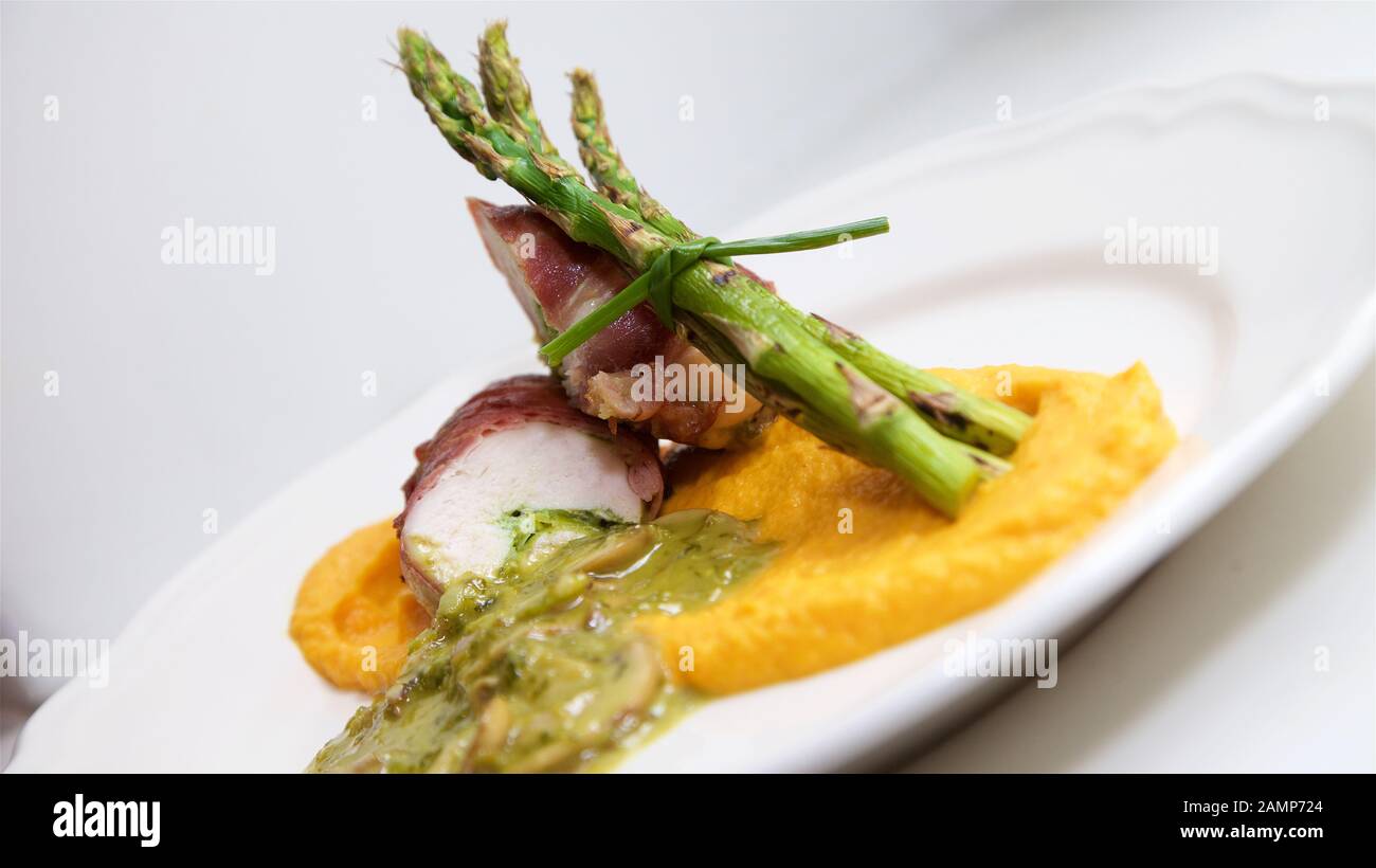 Plato principal, un restaurante de pollo envuelta en jamón de Parma servido con espárragos, setas y puré de camote. Foto de stock