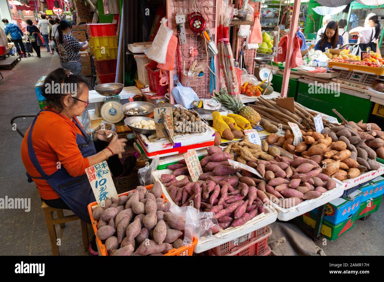 Una mujer comerciante de mercado o vendedor que trabaja en su puesto de venta de hortalizas de raíz para alimentos, Bowring Street mercado, Kowloon Hong Kong Asia Foto de stock