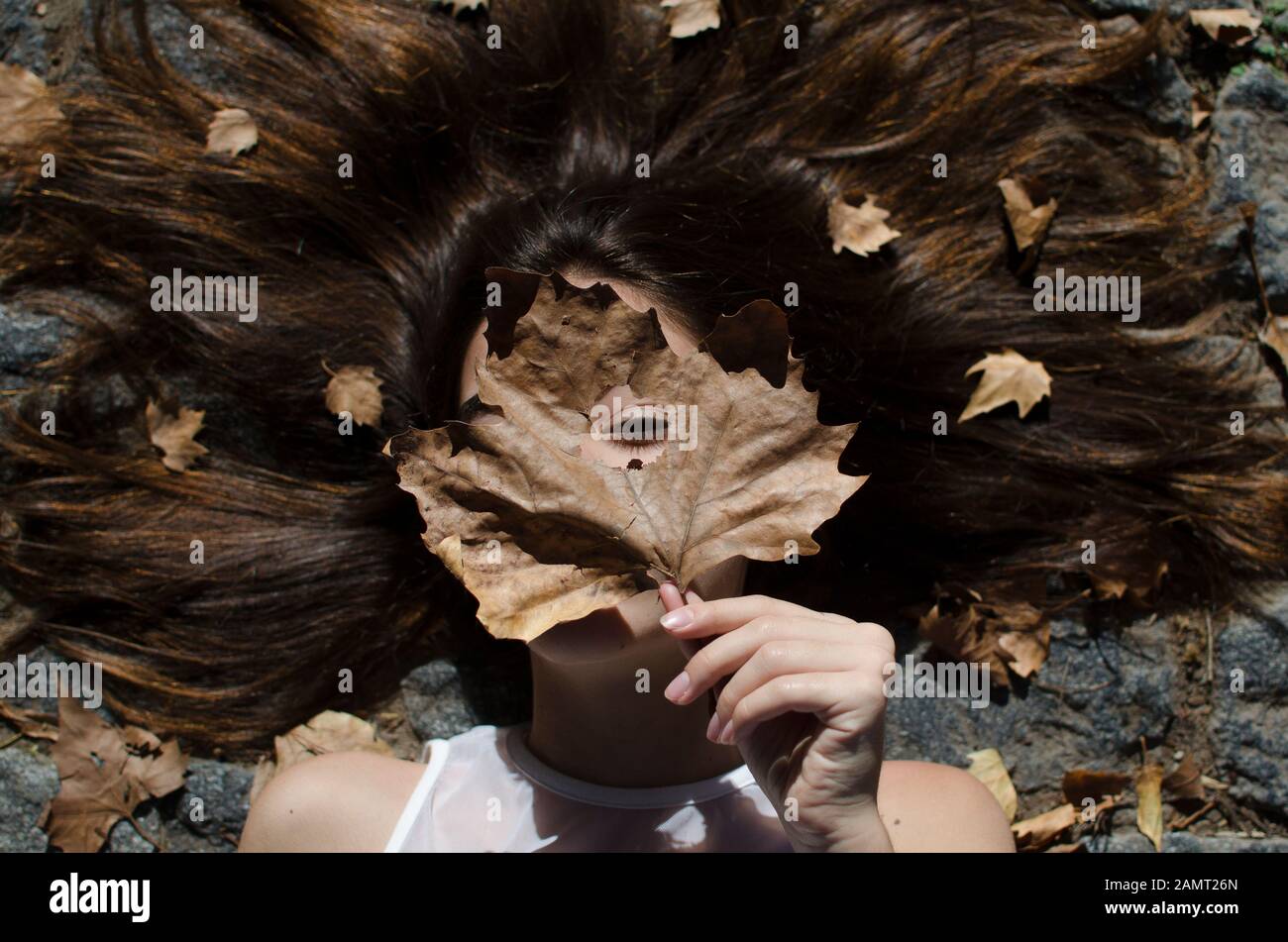 Niña adolescente acostada en el suelo con hojas en su cabello Foto de stock