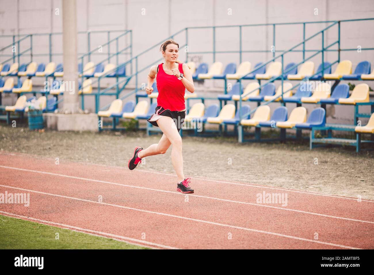 Corredor femenino para correr en pista de estadio, atleta corriendo y haciendo ejercicio al aire libre, deporte concepto fitness. Mujer joven en el entrenamiento de ropa deportiva Fotografía de