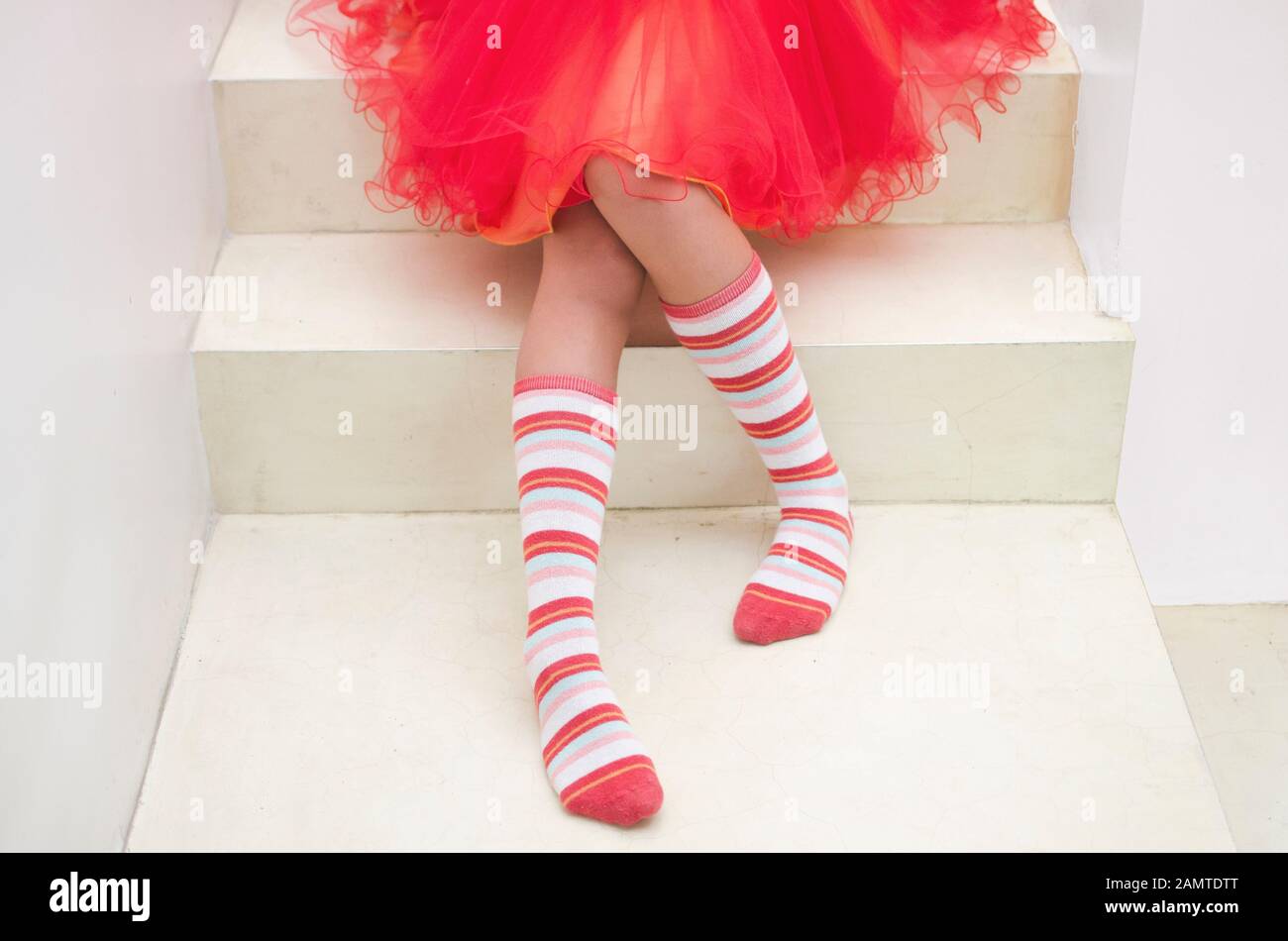 Hermosa niña en marrón suéter y en rayas calcetines largos sentarse en el  piso, aislado en blanco Fotografía de stock - Alamy