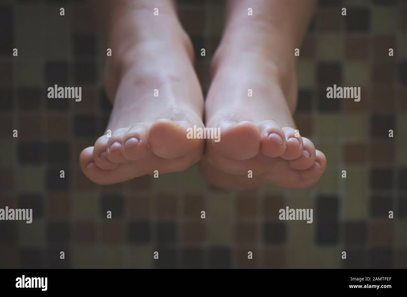 Primer plano de los pies de una niña colgando sobre el borde de un baño Foto de stock