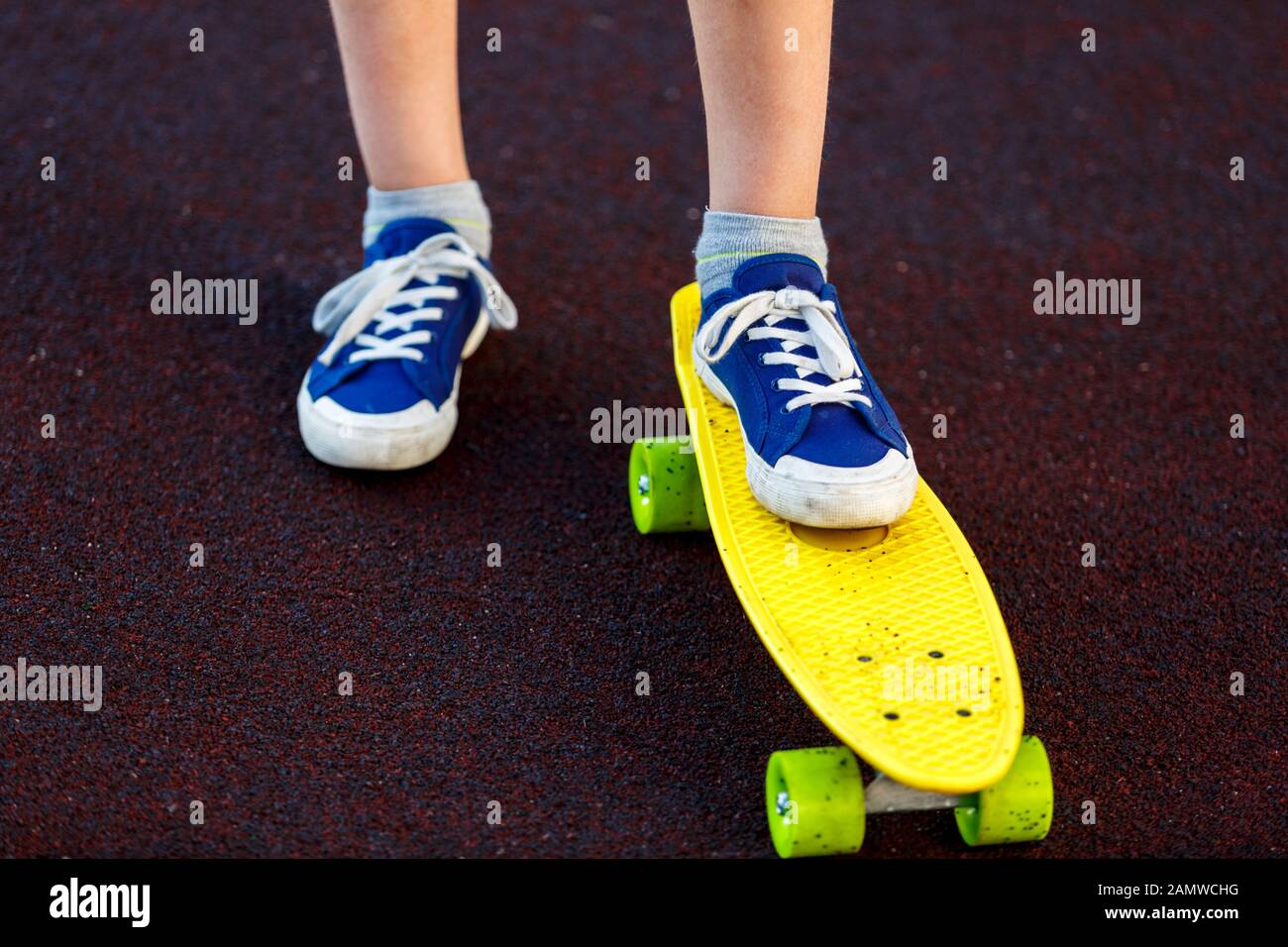 Cierra las piernas en unas sneakers azules que se montan en el skateboard amarillo en movimiento. Estilo de vida urbano activo de la juventud, entrenamiento, afición, concepto de la actividad. Salida activa Foto de stock