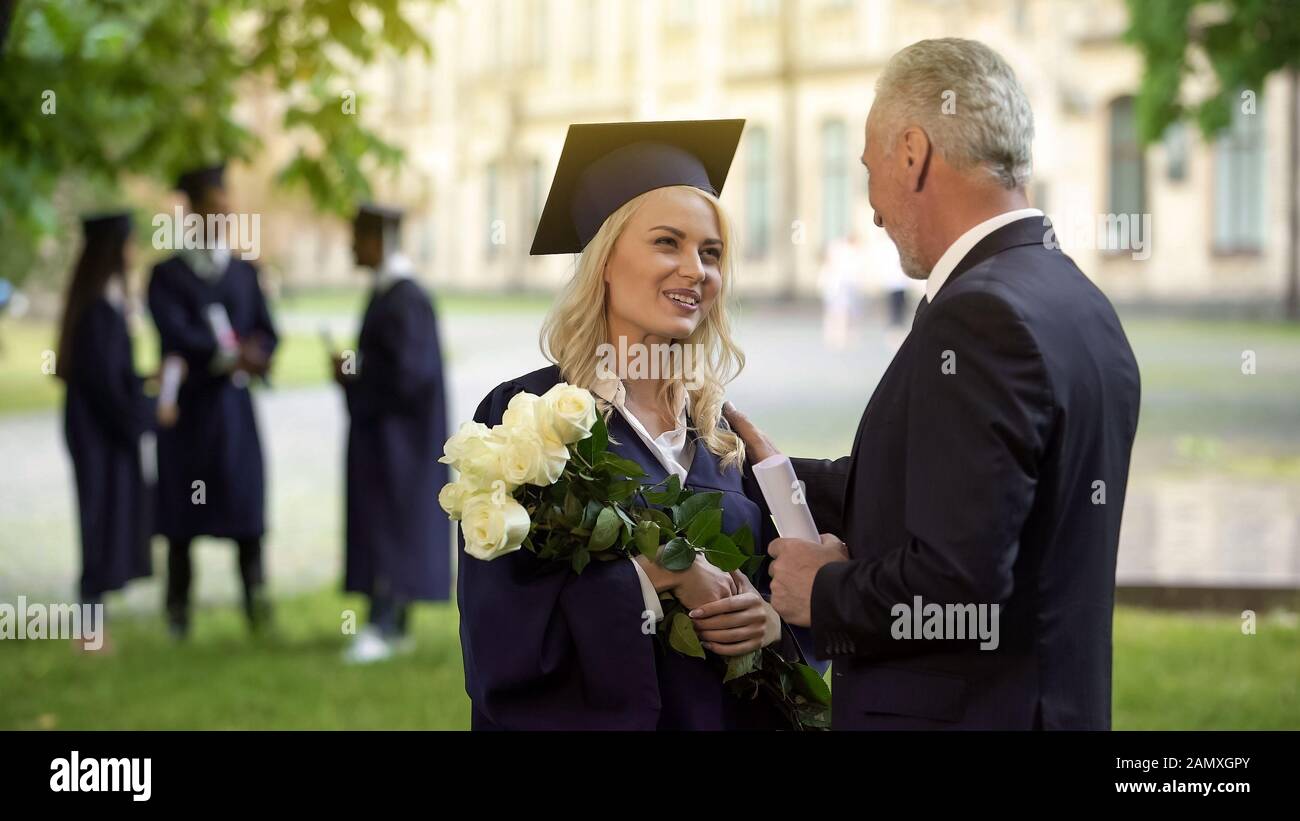 Padre dando flores a su hija graduada, felicitaciones, orgullo paterno Foto de stock