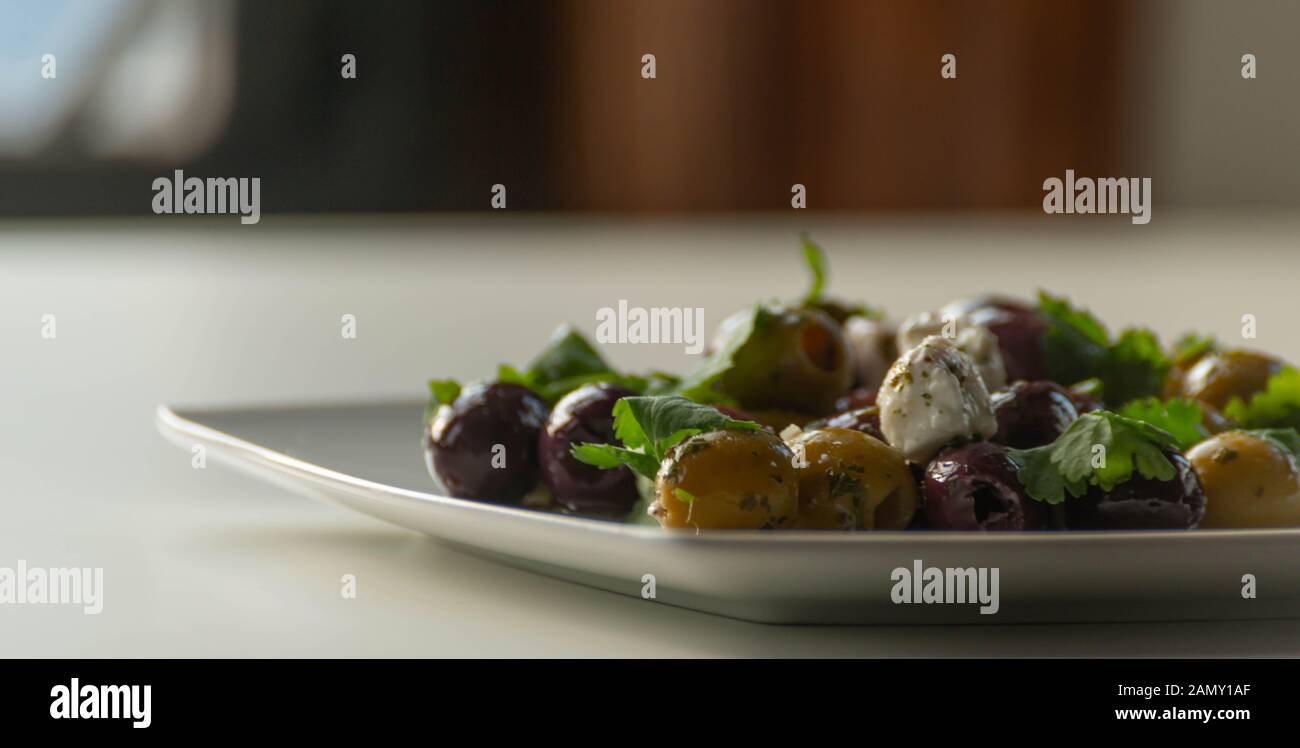 Fresca ensalada griega sobre la base de aceitunas verdes y negras, con trozos de queso blanco y perejil, cocina tradicional mediterránea. Foto de stock