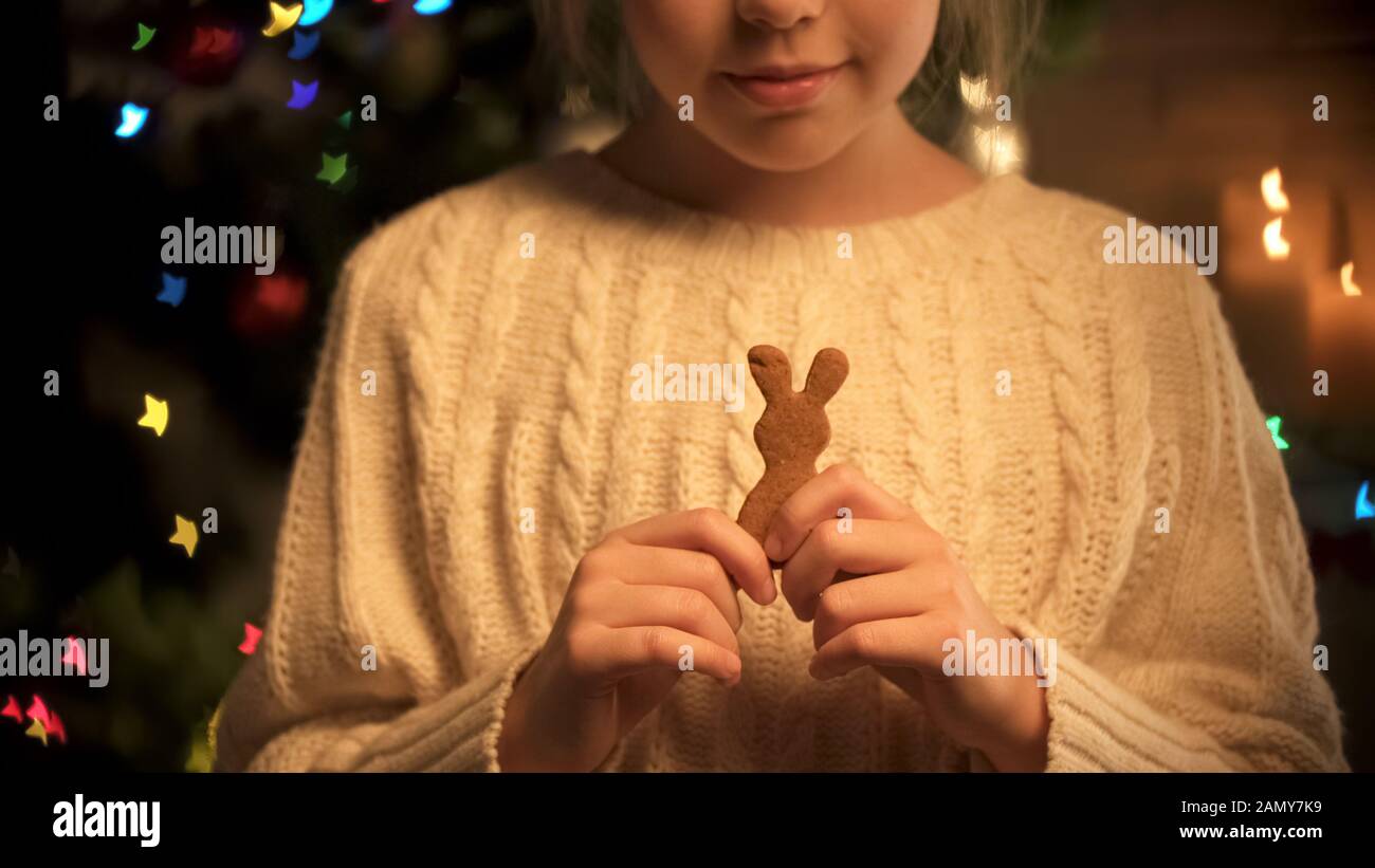 Linda chica con sabrosa galleta de jengibre en las manos de pie sobre fondo festivo Foto de stock