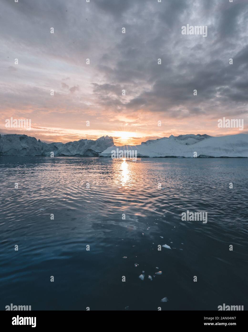 Naturaleza del paisaje ártico con icebergs en Groenlandia icefjord con sol de medianoche atardecer amanecer en el horizonte. Temprano en la mañana de verano durante alpenglow Foto de stock