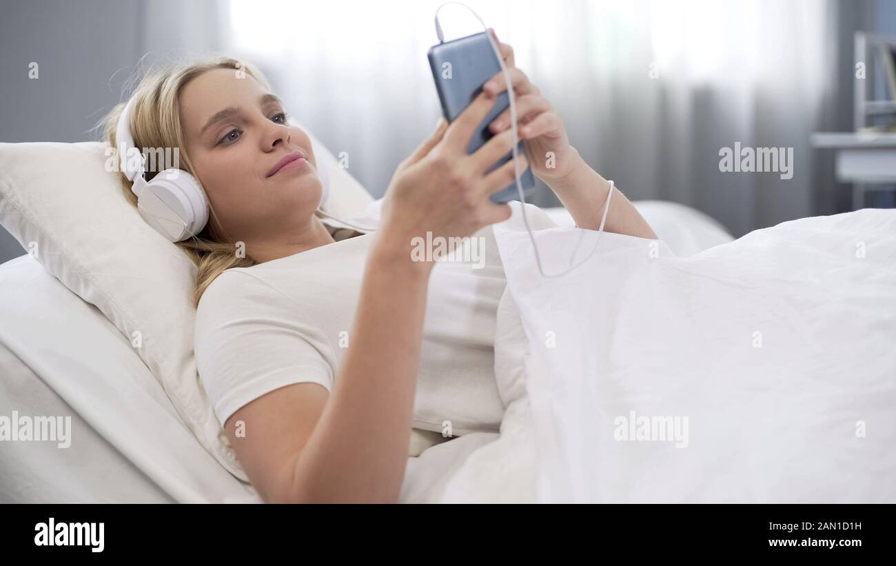 Adolescente en auriculares escuchando música en la cama, comunicándose en las redes sociales Foto de stock