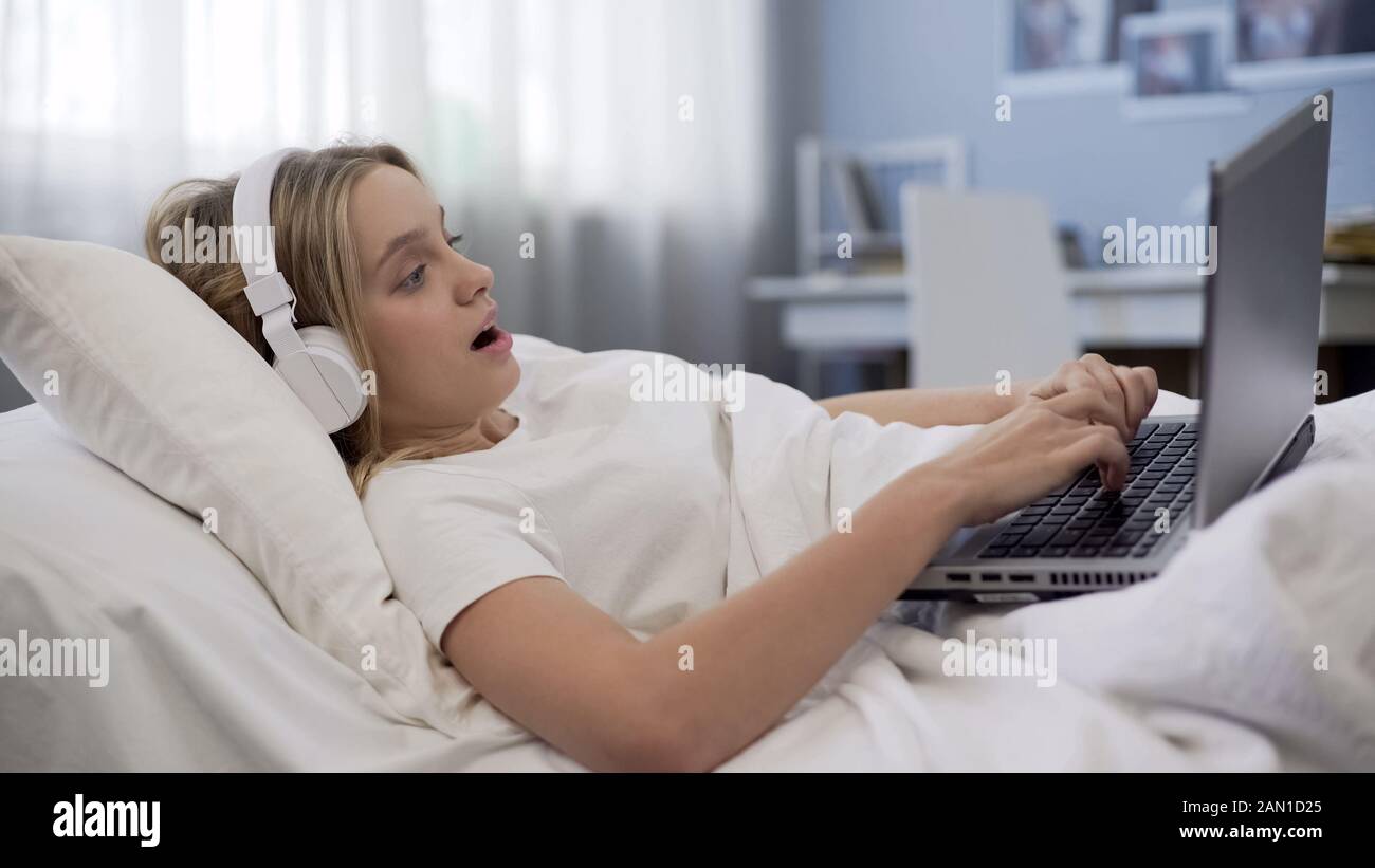 Asombrado adolescente en los auriculares viendo contenido multimedia en línea con el portátil Foto de stock