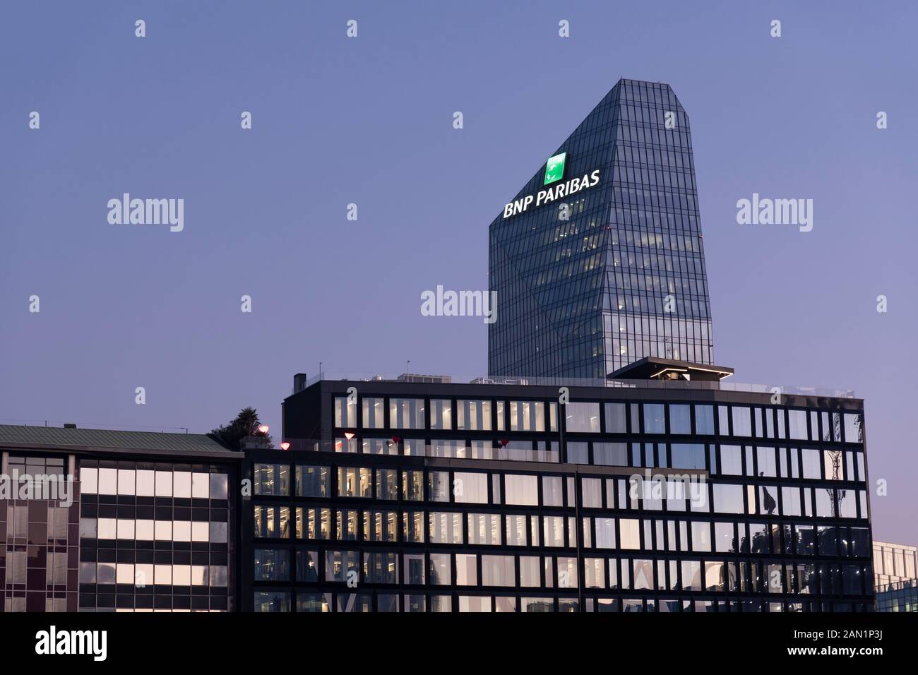 Edificio de vidrio, sede del banco francés BNP Paribas con el logotipo cartel iluminado al atardecer. Milán, Italia. Foto de stock