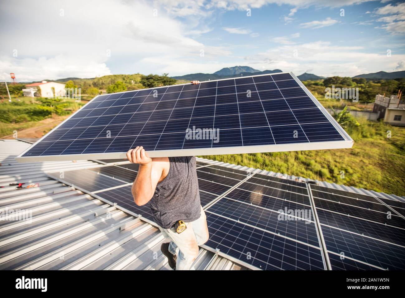 El hombre lleva el panel solar sobre su cabeza durante la instalación. Foto de stock