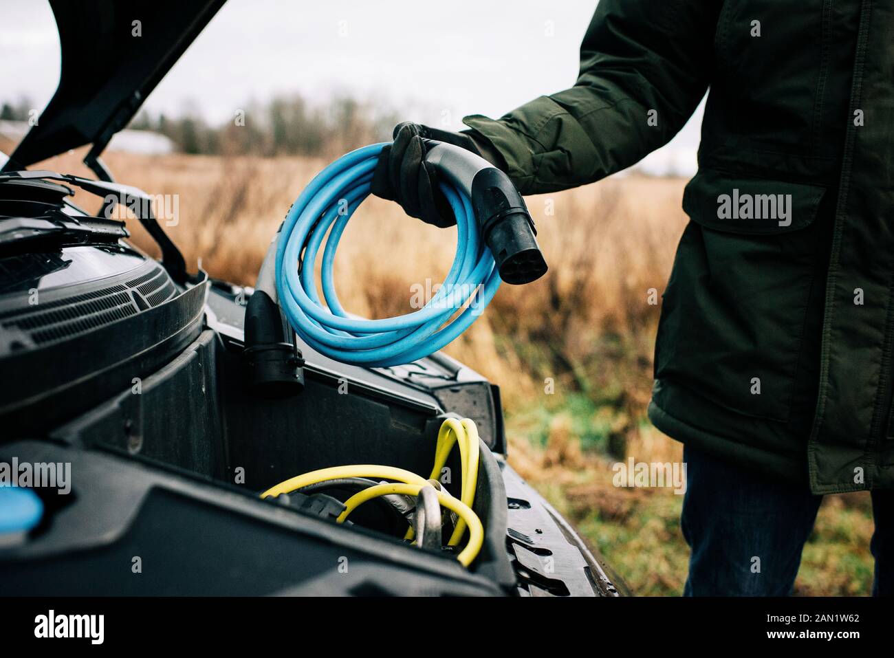 hombre poniendo un cable eléctrico en la capucha de un coche eléctrico Foto de stock