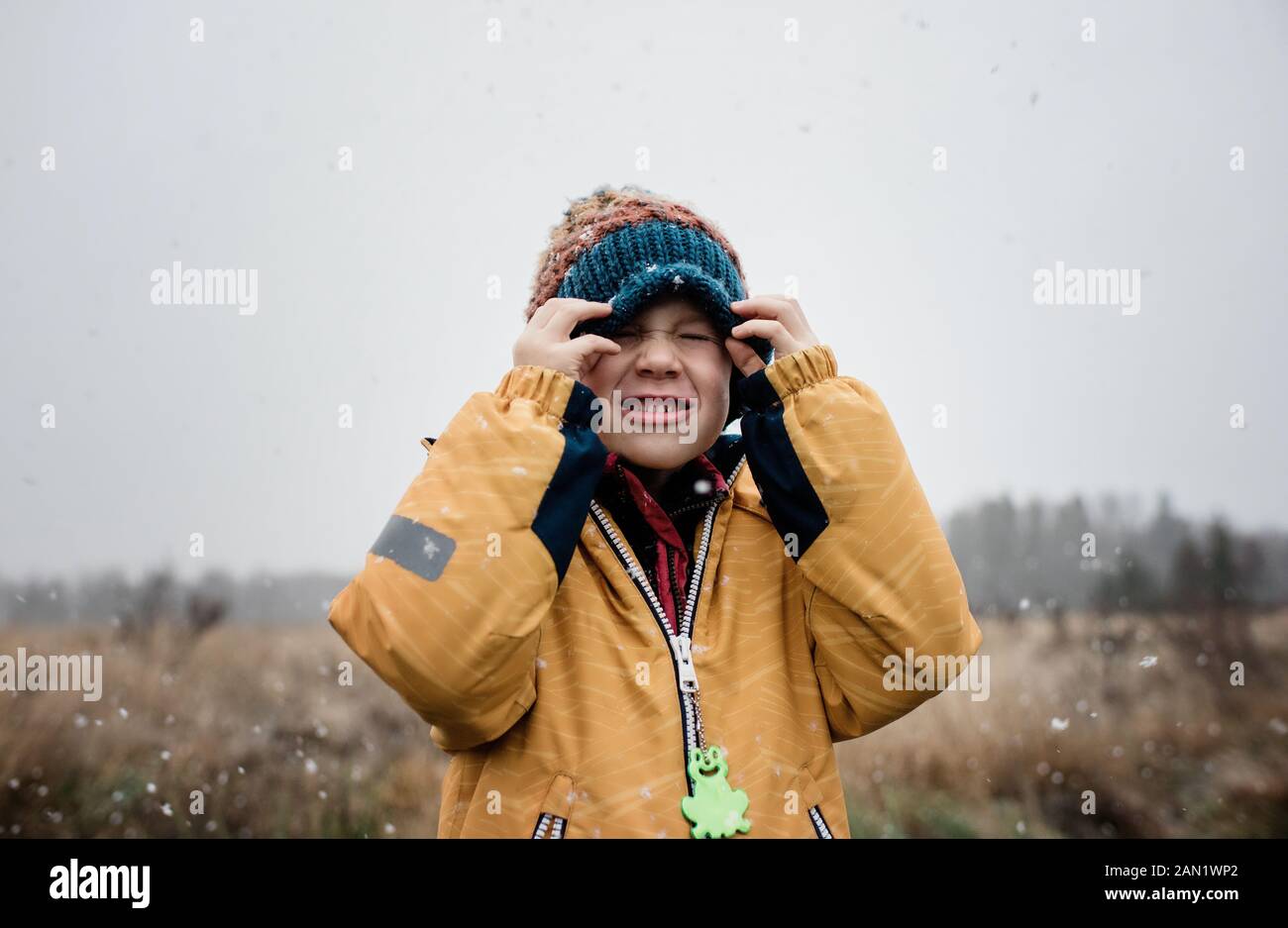 niño cubriendo su cara con su sombrero mientras juega en la nieve Foto de stock