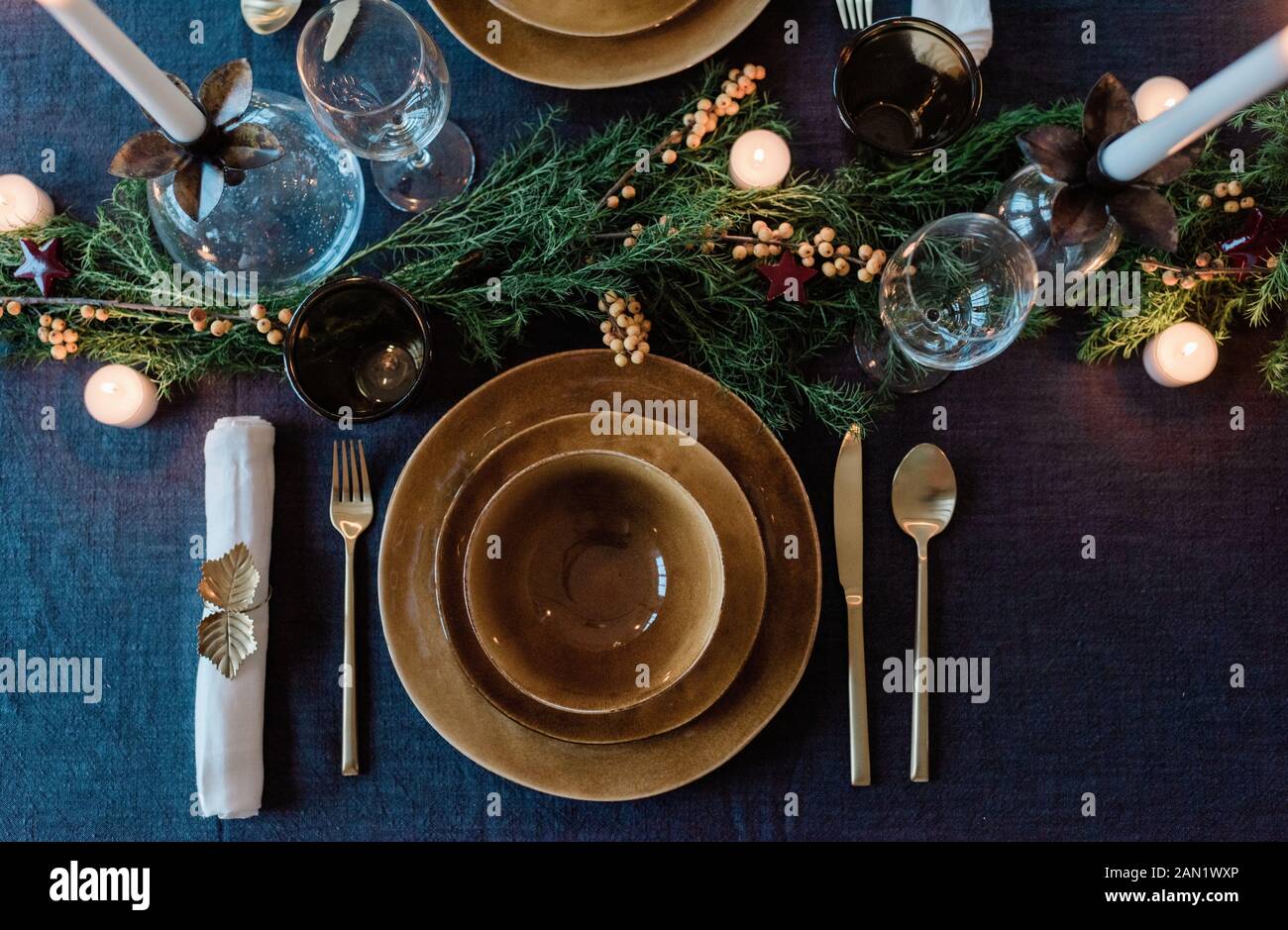 platos dorados y cubiertos en una mesa de cena decorada con vegetación Foto de stock
