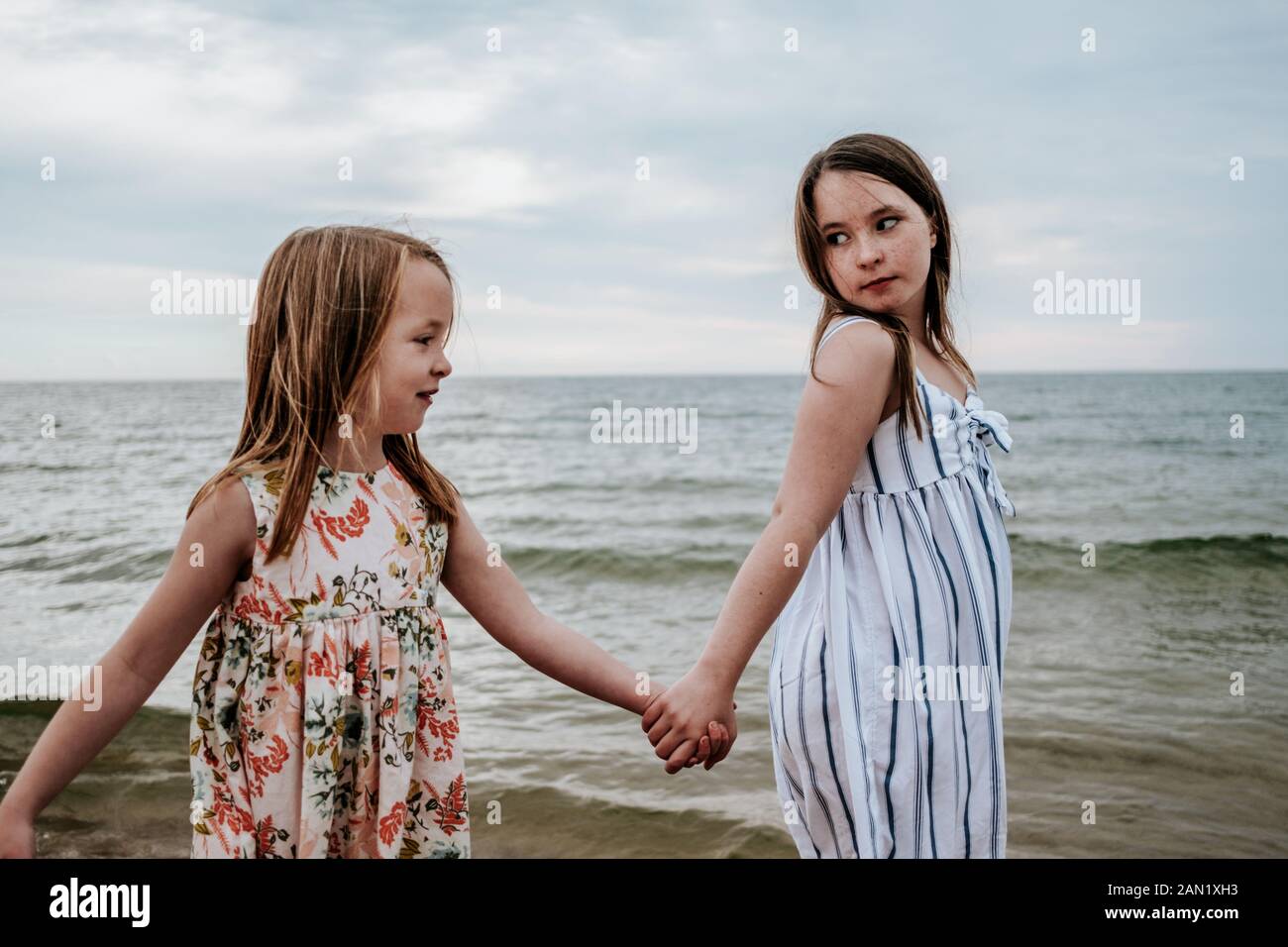 retrato de hermanas sosteniendo las manos y caminando cerca de un lago Foto de stock