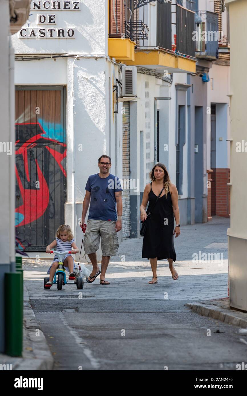 Los padres siguen pacientemente a una niña montando su trike en una calle tranquila de Sevilla Foto de stock