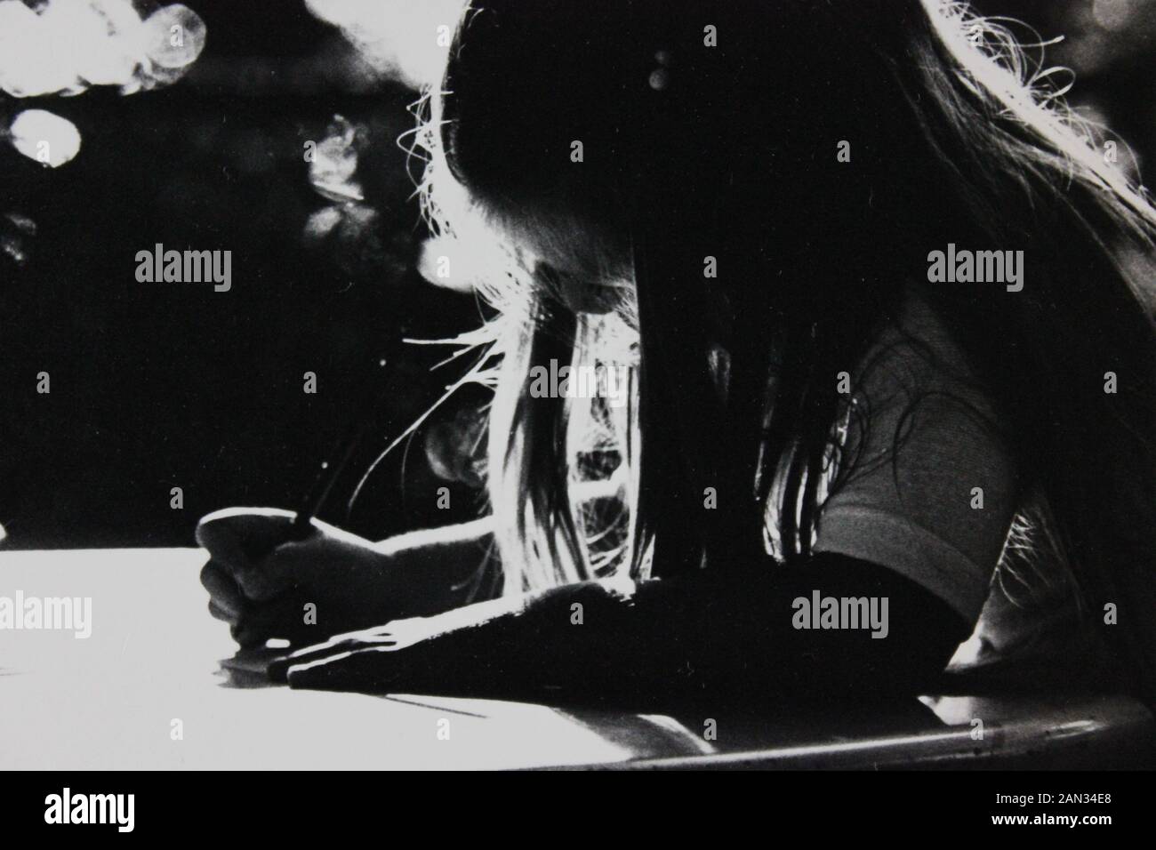 Fotografía extrema blanca y negra de los años setenta de niña escribiendo en un escritorio con retroiluminación Foto de stock