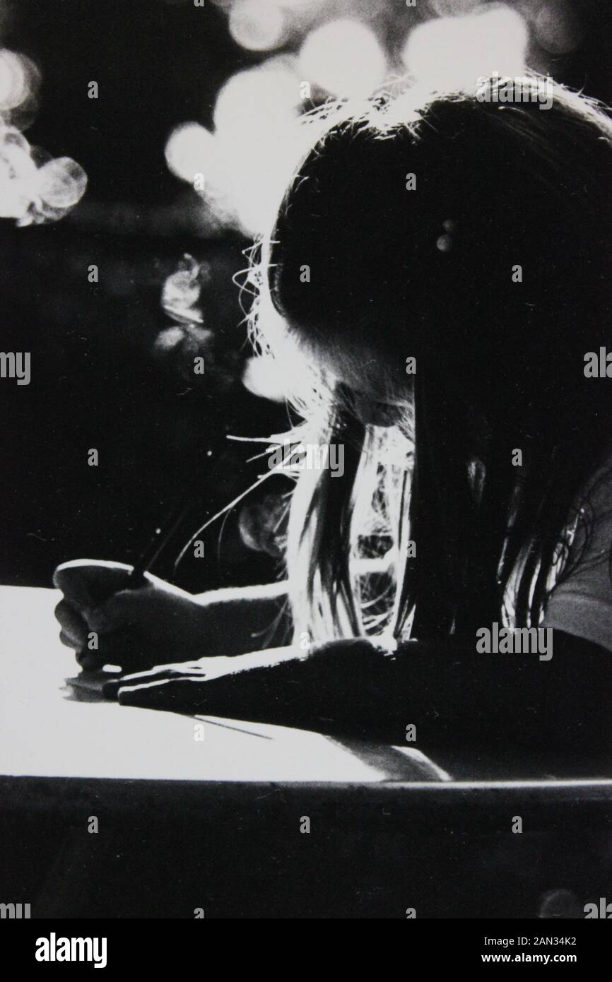 Fotografía extrema blanca y negra de los años setenta de niña escribiendo en un escritorio con retroiluminación Foto de stock