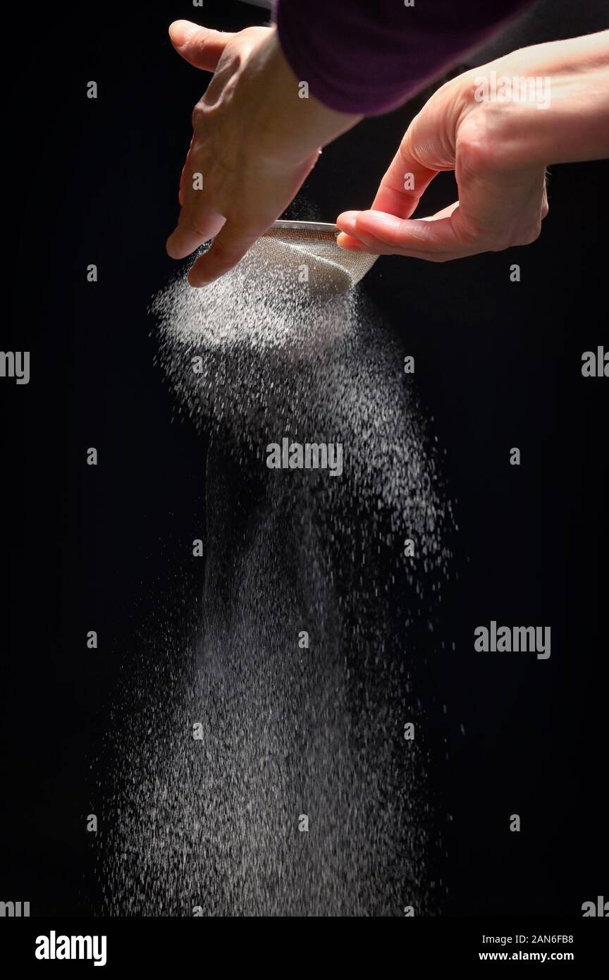 Azúcar en polvo salpica por mujer mano sobre fondo negro Foto de stock