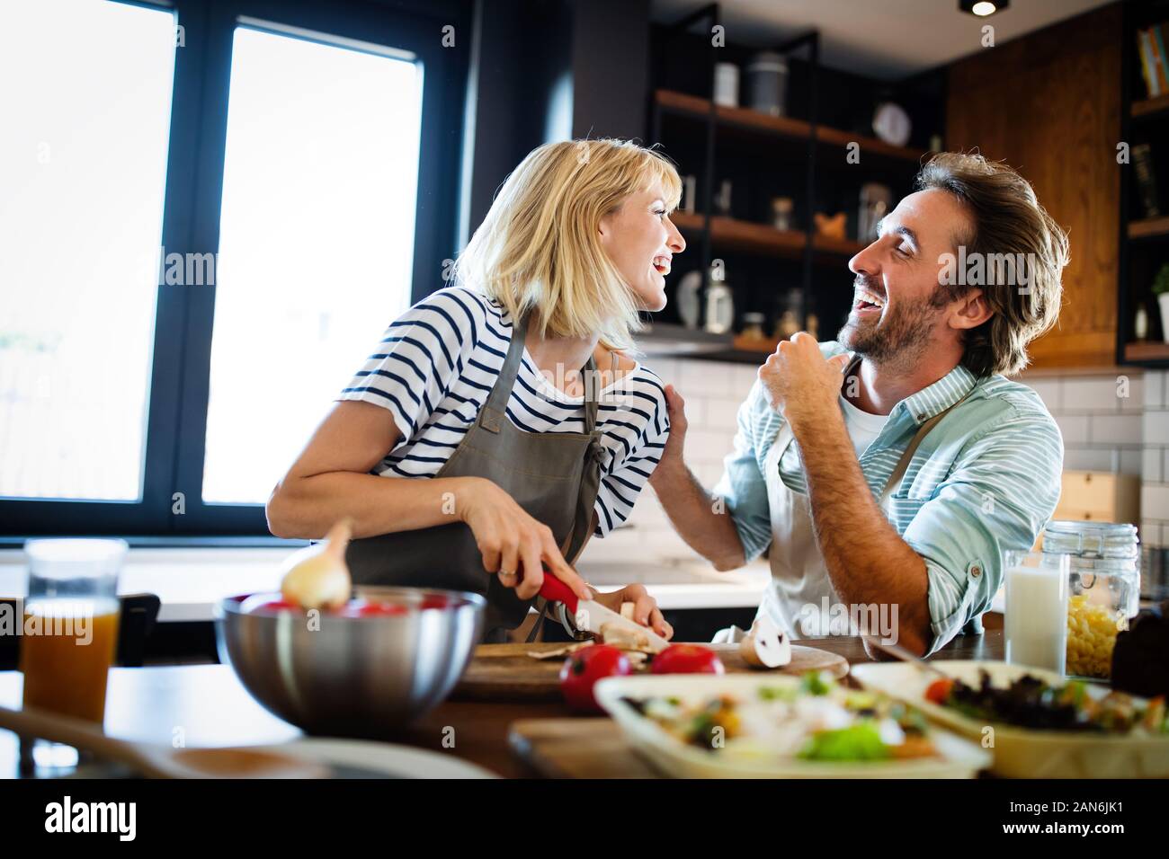 Hermosa pareja joven está hablando y sonriendo mientras se cocina la comida sana en la cocina de casa Foto de stock