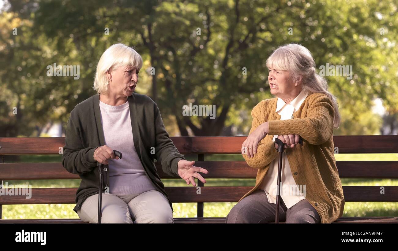 Dos altos señoras argumentando y sentado en banco en parque, grumpy ancianos, disputa Foto de stock