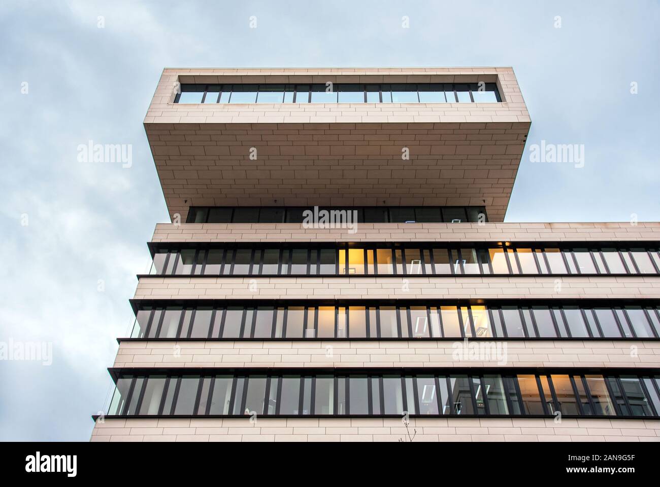 La arquitectura de diseño moderno edificio de oficinas con balcón en la parte superior, visto desde un ángulo bajo contra el cielo nublado Foto de stock