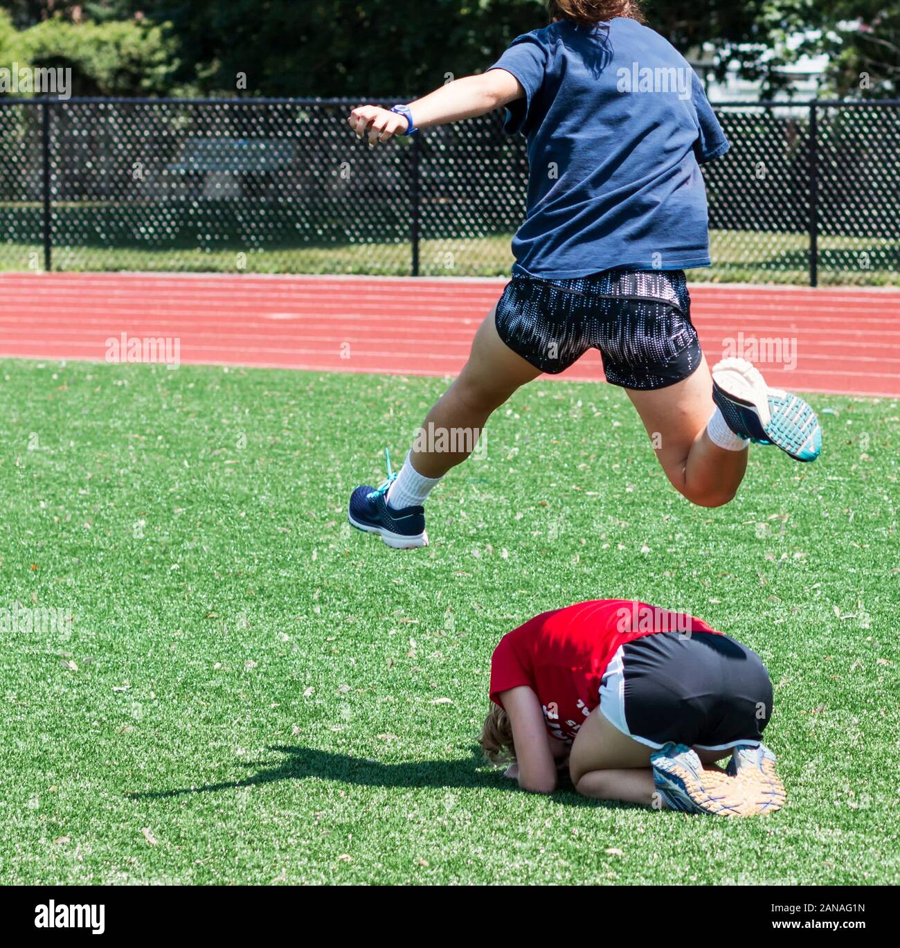 En una escuela secundaria de atleta de pista y campo obstáculos a su compañero de equipo durante una partida de Leap Frog en una divertida jornada práctica en el verano. Foto de stock