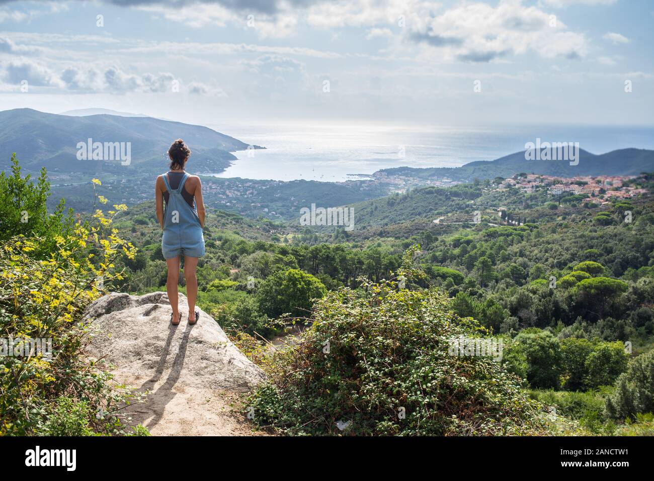 Mujer joven admirando el panorama de hill supervisa bay en Toscana vistiendo denim dungaree Foto de stock