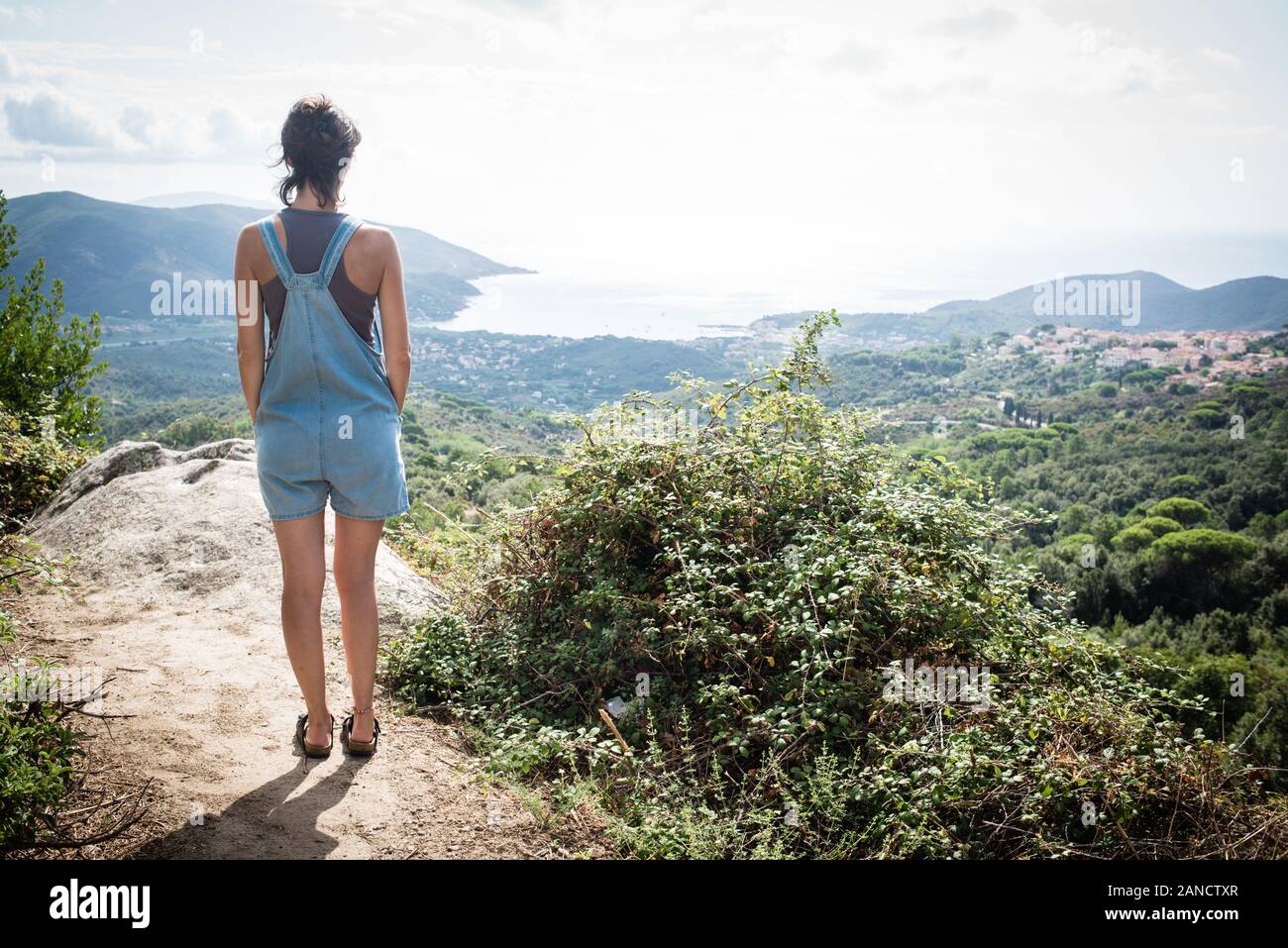 Mujer joven admirando el panorama de hill supervisa bay en Toscana vistiendo denim dungaree Foto de stock