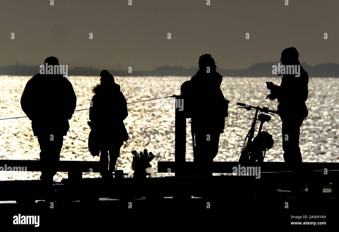 Las personas en silueta y el sol brillante en el extremo de un muelle junto al mar. Foto de stock