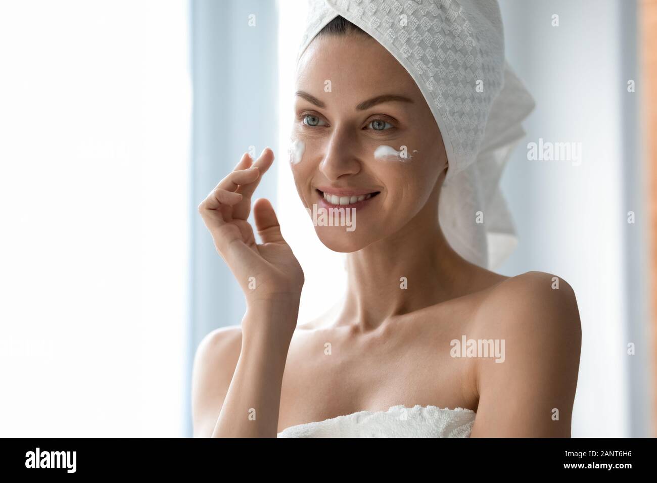 Hermosa mujer con sonrisa saludable aplicar crema en mejillas Foto de stock
