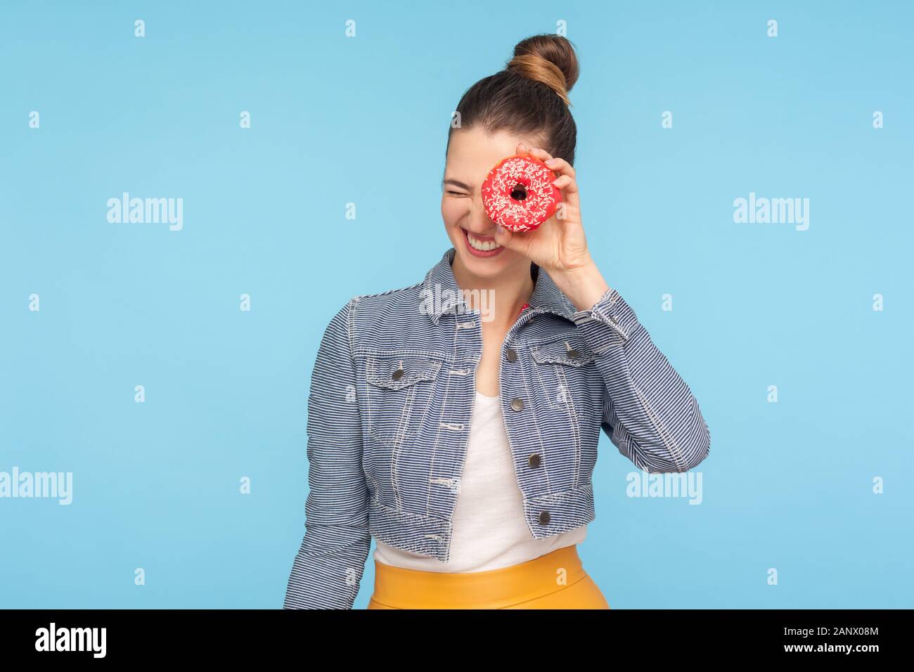 Encantado de niña despreocupada, en traje de moda mirar a través de donut hole y sonriente, divertirse con snack, mirando a donut, azucarados confectione Foto de stock