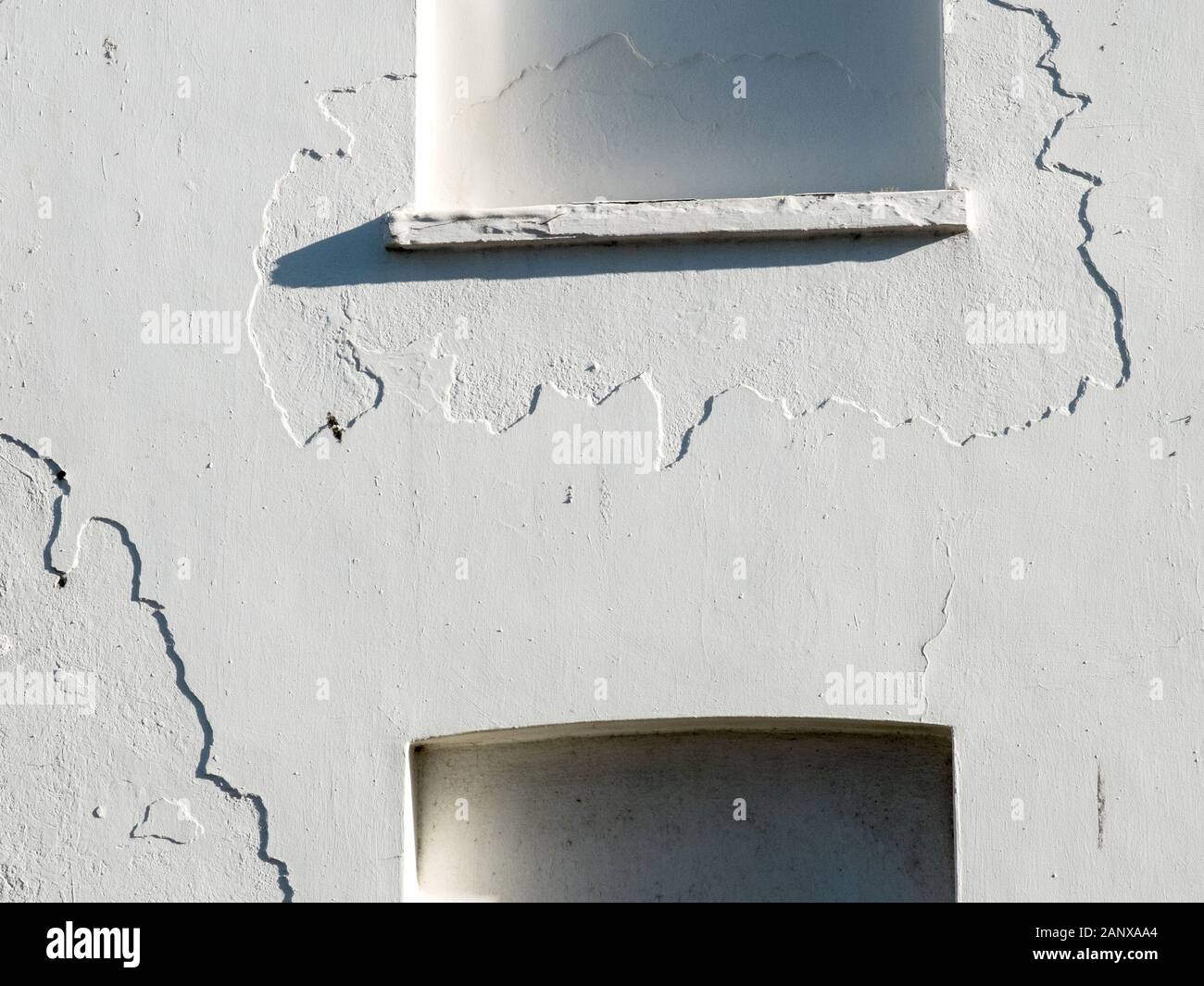 Los detalles de la pared blanca agrietada del yeso rodean las ventanas bloqueadas en una casa derelict en Clacton en el mar, Essex, Reino Unido Foto de stock