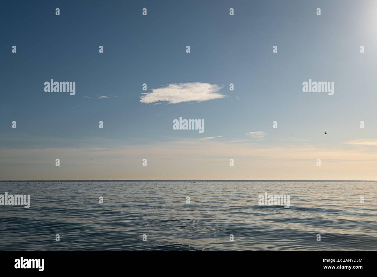 vista panorámica del horizonte sobre el mar tranquilo con una nube en el cielo durante la hora dorada Foto de stock