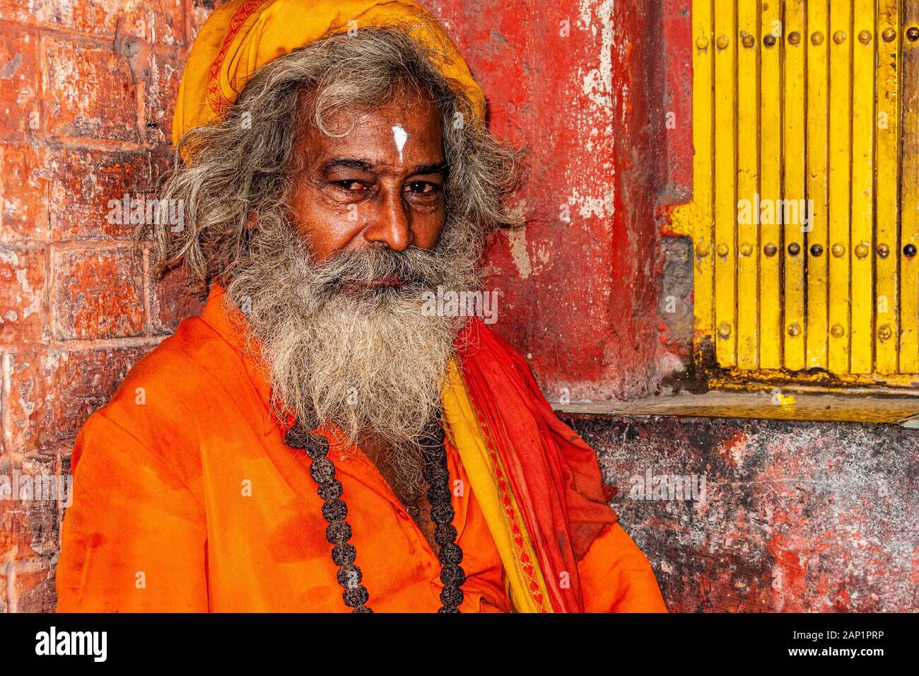 Un Sadhu, hombre santo, usando paños de naranja, sentado frente a un pequeño santuario Foto de stock