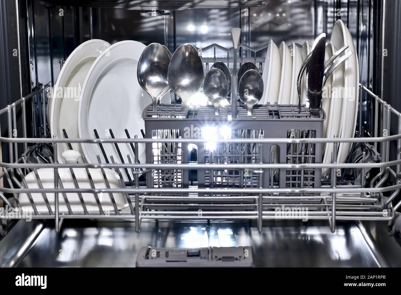 La bandeja inferior de la cesta de lavavajillas se empuja hacia adelante en forma ordenada llena con pura utensilios de espumoso. Foto de stock
