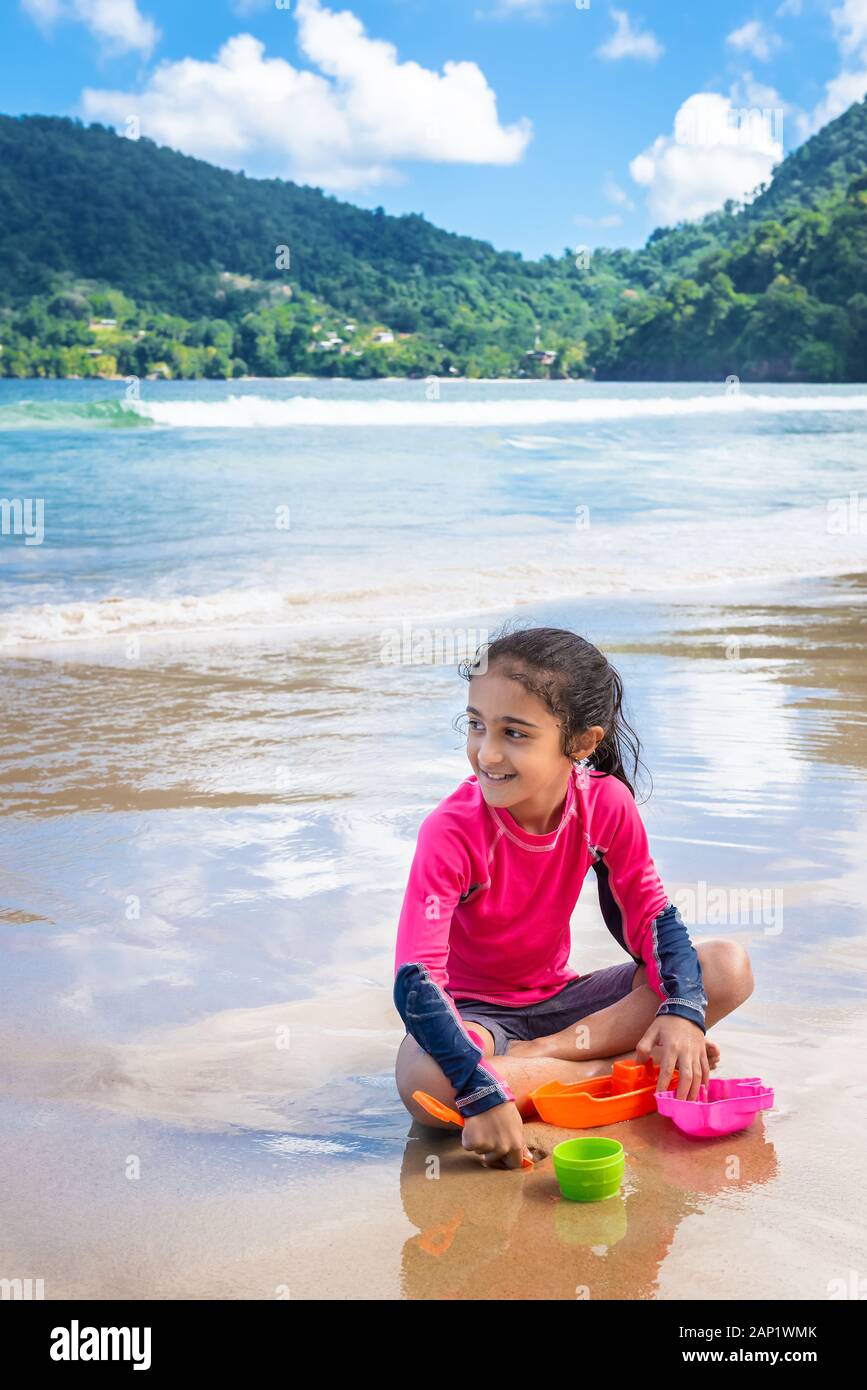 Niña jugando con arena en las Maracas Bay Beach Trinidad y Tobago sentados al aire libre actividad divertida sonriente Foto de stock