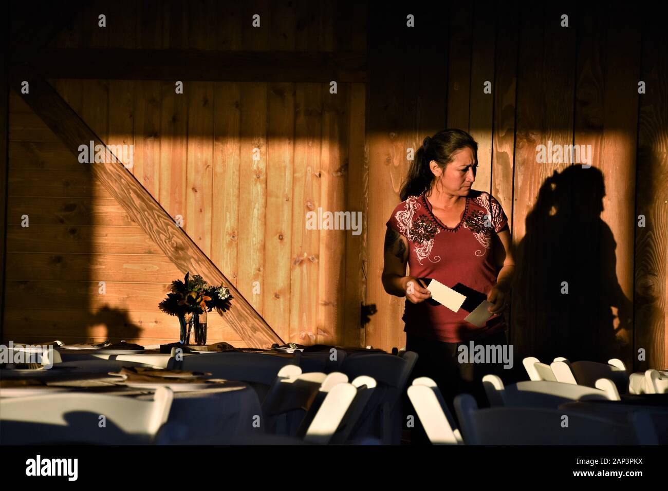 Edad media mujer étnica hispana mesa de decoración antes de una boda recepción en un granero para familiares con tarjetas de lugar con nombres Foto de stock